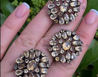 May include: Three silver rings with a cluster of light brown gemstones. The rings are on a finger.