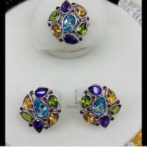 May include: A silver ring and matching earrings set. The ring and earrings feature a cluster of colorful gemstones in shades of blue, yellow, green, purple, and red. The gemstones are arranged in a floral pattern.