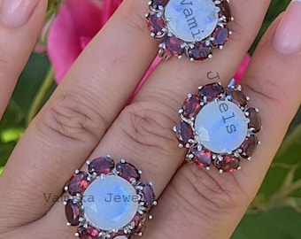 May include: Three silver rings with a floral design. Each ring features a large, round, light-colored stone surrounded by smaller, oval, dark red stones. The rings have the text "Vamika Jewels" on them.