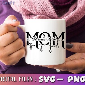 May include: White ceramic mug with a black design that says "MOM thank you" with a string of lights and diamonds hanging from the letters.