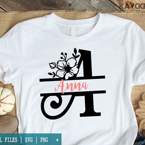 May include: A white t-shirt with a black floral design and the name "Anna" written in pink. The design features a large letter "A" with a floral design and a horizontal line with the name "Anna" written on it.