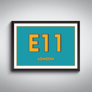 May include: Framed wall art featuring the text "E11 LONDON" in orange on a teal background. The artwork is encased in a black frame with a white border, creating a modern and minimalist aesthetic. The artwork is mounted on a light gray wall.