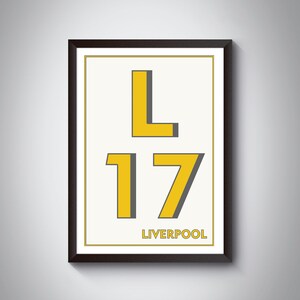May include: A framed print with a white background and black frame. The print features the letters "L" and "17" in yellow with a gray outline. The word "LIVERPOOL" is printed in black below the numbers.