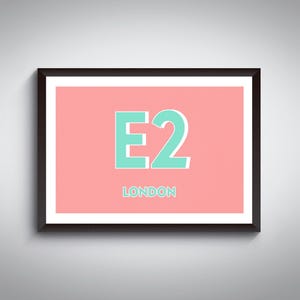 Può includere: Stampa artistica incorniciata con la scritta "E2 LONDON" in turchese su sfondo corallo. L'opera è racchiusa in una cornice nera con bordo bianco, creando un'estetica moderna e minimalista. La stampa è montata su una parete grigio chiaro.