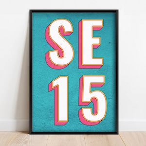 May include: A framed art print featuring the text "SE 15" in a bold, 3D style. The letters and numbers are white with pink and yellow outlines, set against a textured teal background. The frame is black.