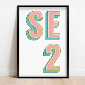 Könnte beinhalten: Ein gerahmter Druck mit dem Text "SE2" in rosa Buchstaben mit türkisfarbenem Umriss. Die Buchstaben sind in einer Schriftart im Retro-Stil.