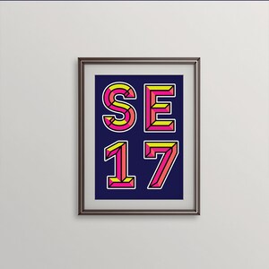 May include: A framed print with a navy blue background featuring the text "SE 17" in bold, pink and yellow 3D letters.