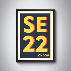 May include: A framed print with a navy blue background and yellow text that reads "SE22 LONDON". The text is outlined in red.