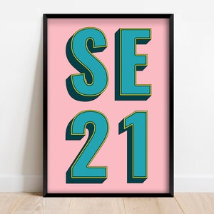 Könnte beinhalten: Gerahmter Kunstdruck mit dem Text "SE 21" in Türkis, umrandet von Gelb, auf rosa Hintergrund. Die fetten Buchstaben im 3D-Stil sind in einem schwarzen Rahmen gesetzt und erzeugen einen auffälligen Kontrast.