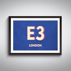 Puede incluir: Arte mural enmarcado con el texto "E3 LONDON" en crema sobre fondo azul. La obra está encerrada en un marco negro con borde blanco. El diseño es simple y audaz, adecuado para interiores modernos. Una pieza de decoración de pared elegante.