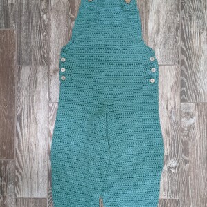 May include: Teal crocheted overalls with wooden buttons. The overalls have a wide leg and are cuffed at the bottom.