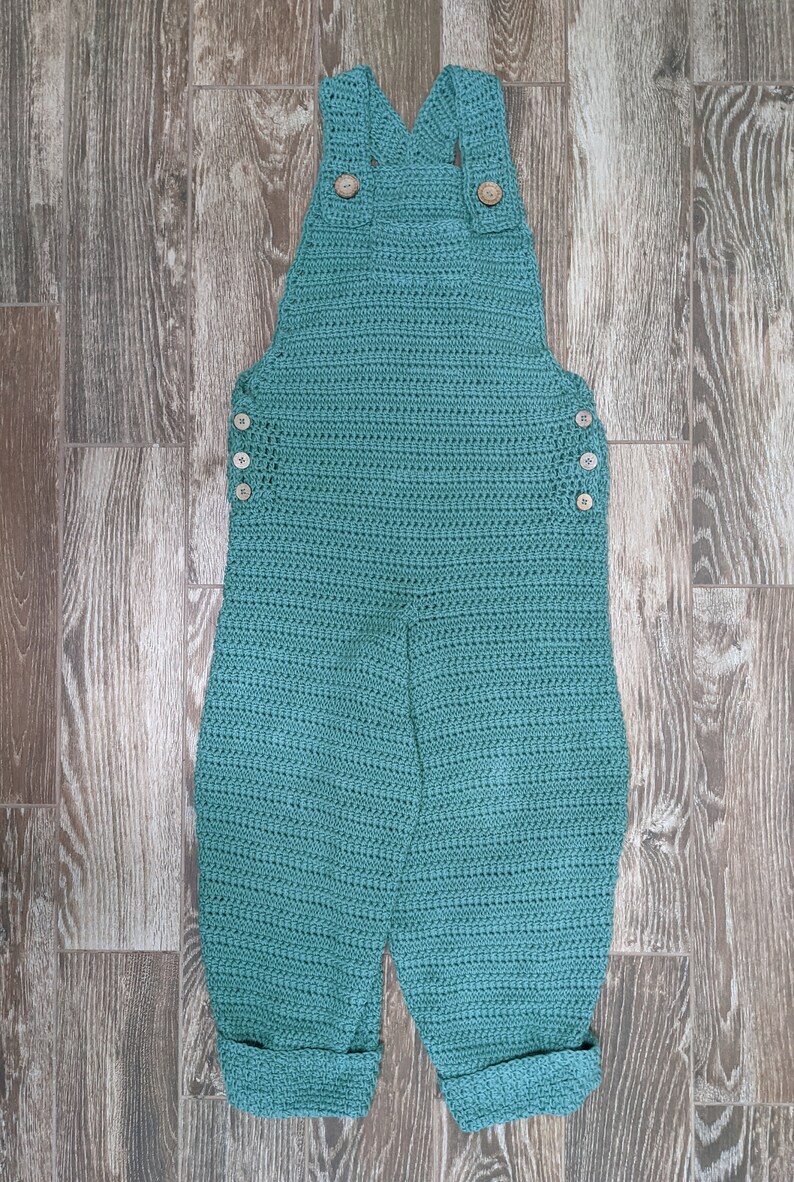 May include: Teal crocheted overalls with wooden buttons. The overalls have a wide leg and are cuffed at the bottom.