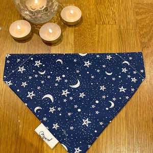 May include: A navy blue dog bandana with a white moon and star pattern. The bandana has a white label with the word "Good" printed on it.