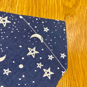 May include: Close-up of a corner of a blue fabric with a white crescent moon and stars pattern.