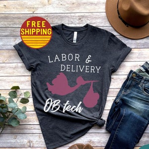 May include: A dark grey t-shirt with the text "Labor & Delivery OB tech" and a pink silhouette of a stork carrying a baby.