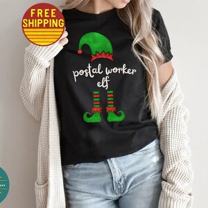 May include: A black t-shirt with a green elf hat and legs, and the text "postal worker elf".