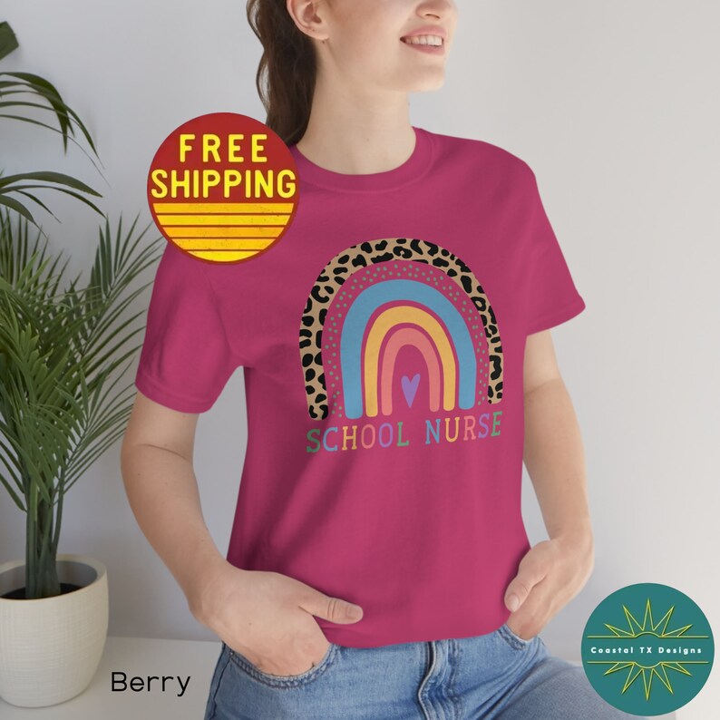 Puede incluir: Una camiseta rosa con un dise&ntilde;o de arco&iacute;ris e estampado de leopardo. El texto "School Nurse" est&aacute; impreso debajo del arco&iacute;ris.