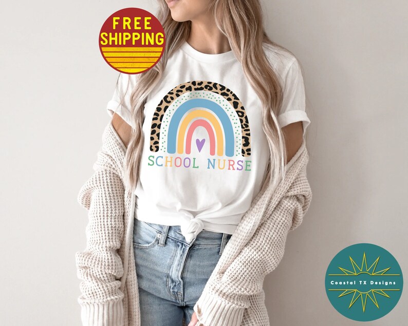 Puede incluir: Camiseta blanca con un dise&ntilde;o de arco&iacute;ris con un borde de estampado de leopardo. El arco&iacute;ris tiene un esquema de color rosa, naranja, amarillo, azul y morado. El texto "SCHOOL NURSE" est&aacute; impreso debajo del arco&iacute;ris.