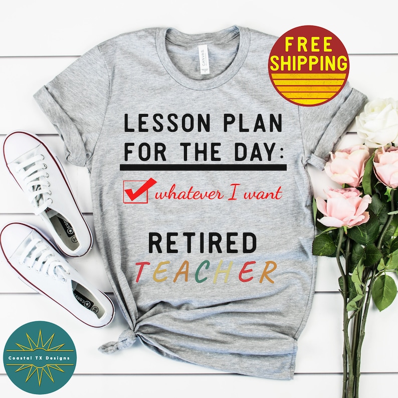 Op de afbeelding: Grijs T-shirt met de tekst "LESSON PLAN FOR THE DAY: whatever I want RETIRED TEACHER" in zwarte en kleurrijke letters. Het woord "RETIRED" is in zwart en het woord "TEACHER" is in regenboogkleuren.