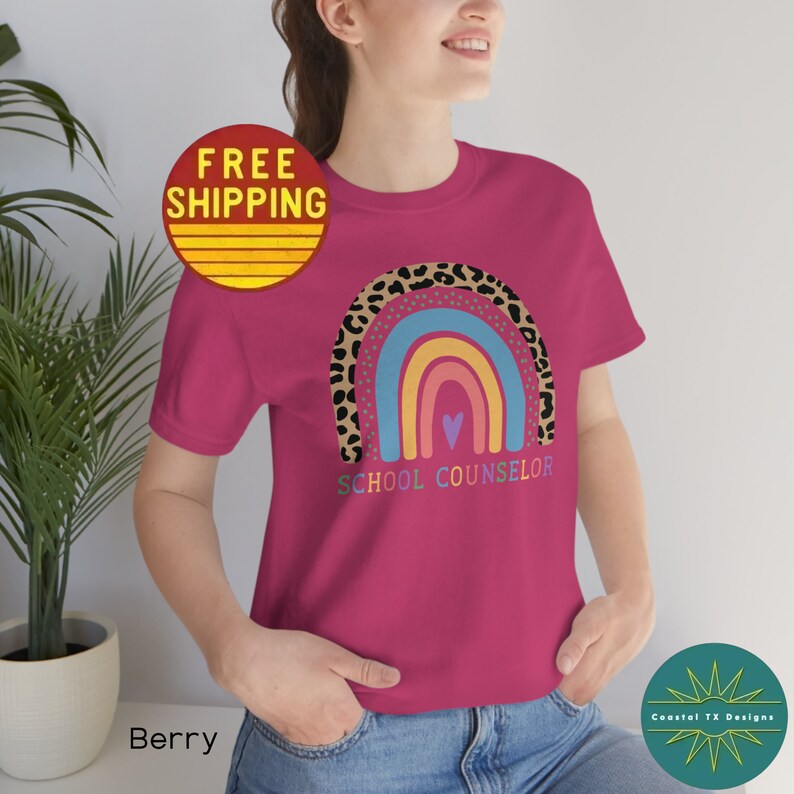 May include: A pink t-shirt with a rainbow design and the text "School Counselor". The rainbow is outlined with a leopard print pattern.