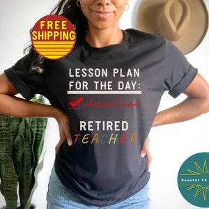 Op de afbeelding: Zwart T-shirt met de tekst "Lesson Plan for the Day:  Whatever I Want" en een vinkje. Onder de tekst staat "Retired Teacher" in regenboogkleuren.