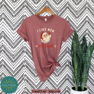 Op de afbeelding: Een heide-paarse t-shirt met een vintage-illustratie van de kerstman die een biertje vasthoudt en de tekst "Ik hou van mannen met baarden".