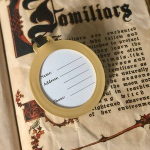 May include: A yellow tag with a round label that says "Name:", "Address:", and "Phone:". The tag is hanging from a book with the word "Familiars" written in black script.