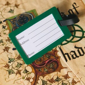 May include: Green luggage tag with a black strap. The tag has blank lines for writing "Name", "Address", and "Phone".