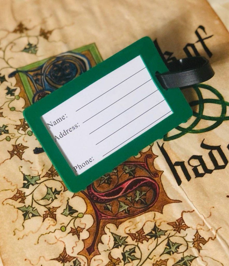 May include: Green luggage tag with a black strap. The tag has blank lines for writing "Name", "Address", and "Phone".