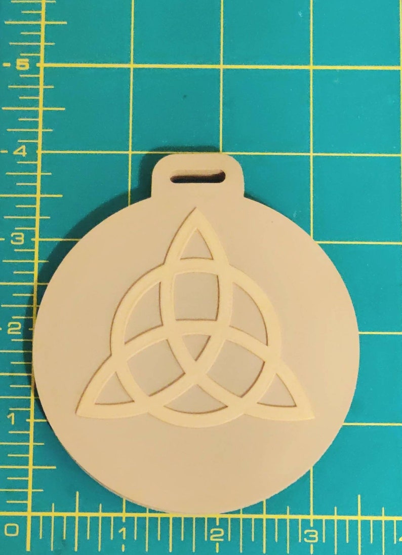 May include: A beige round ornament with a white triquetra symbol. The ornament has a hole at the top for hanging.