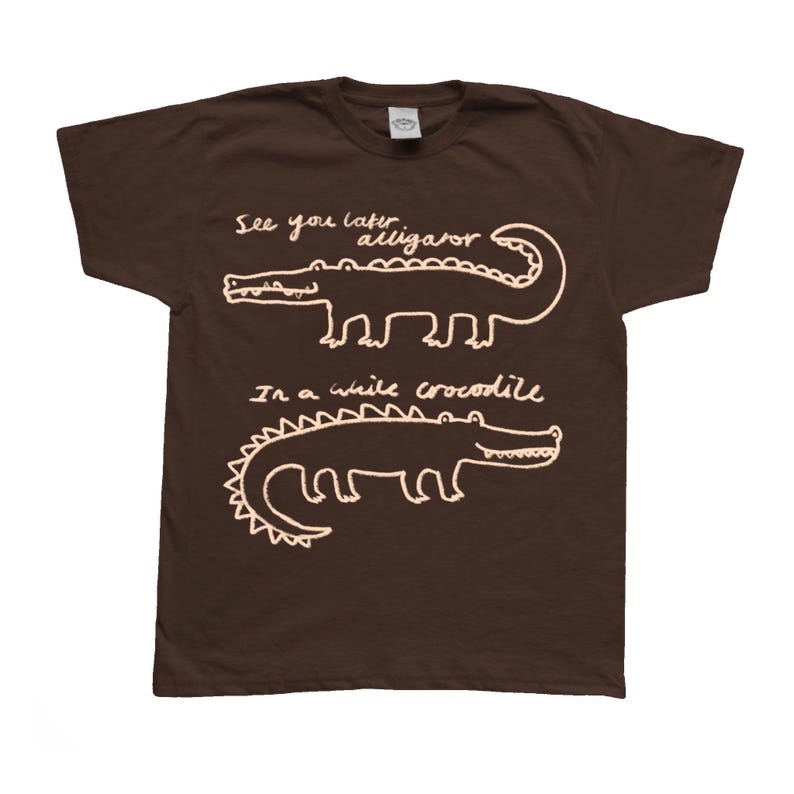 May include: A brown t-shirt with white text and illustrations of two alligators. The top alligator has the text "See you later alligator" above it. The bottom alligator has the text "In a while crocodile" below it.