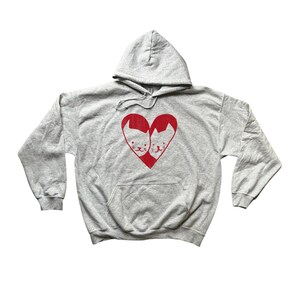 May include: A grey hooded sweatshirt with a red heart design featuring two white cats facing each other.