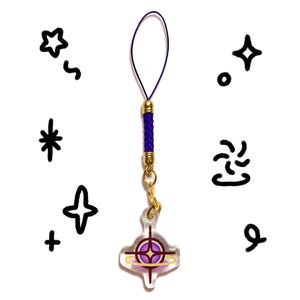 Pu&ograve; includere: Un ciondolo in acrilico trasparente con una grafica circolare viola e oro con una stella centrale, fissato a un cordino intrecciato viola con componenti in metallo dorato. Il ciondolo &egrave; circondato da vari scarabocchi neri disegnati a mano.