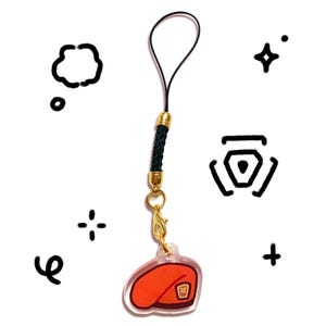 Pu&ograve; includere: Un ciondolo in acrilico trasparente con un design a basco rosso, hardware color oro e un cordino intrecciato nero. Il ciondolo &egrave; attaccato a un fermaglio color oro e un anello nero. Lo sfondo presenta grafiche nere in stile doodle.