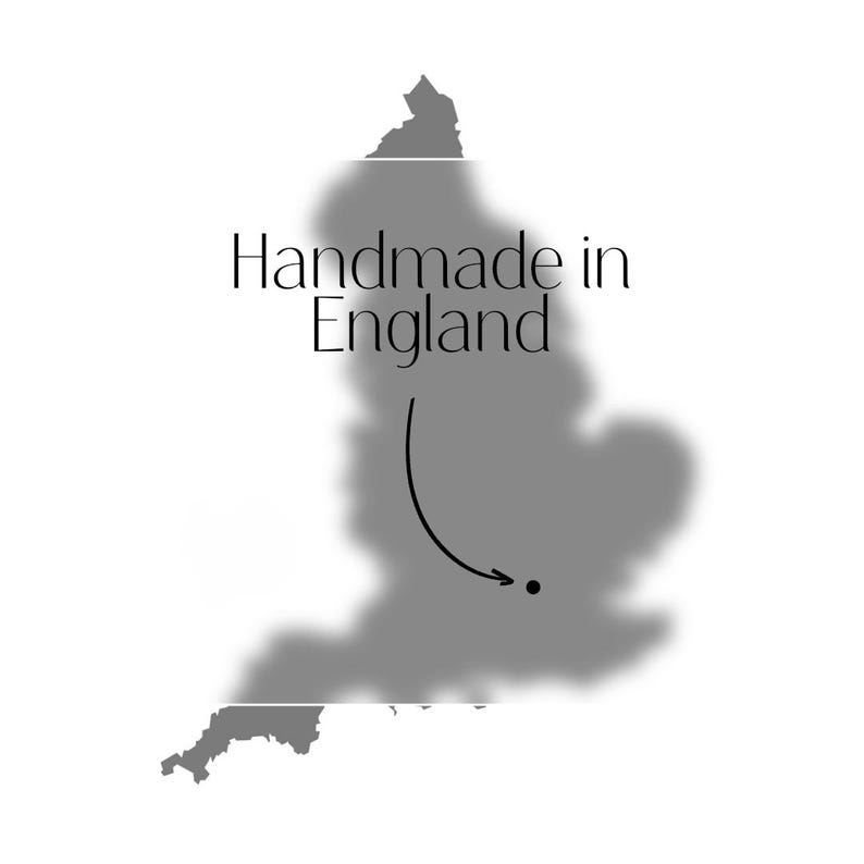 May include: A grayscale image showing the shape of England with the text "Handmade in England." A curved arrow points to a dot on the map. The design is set against a white background, suggesting a product's origin.