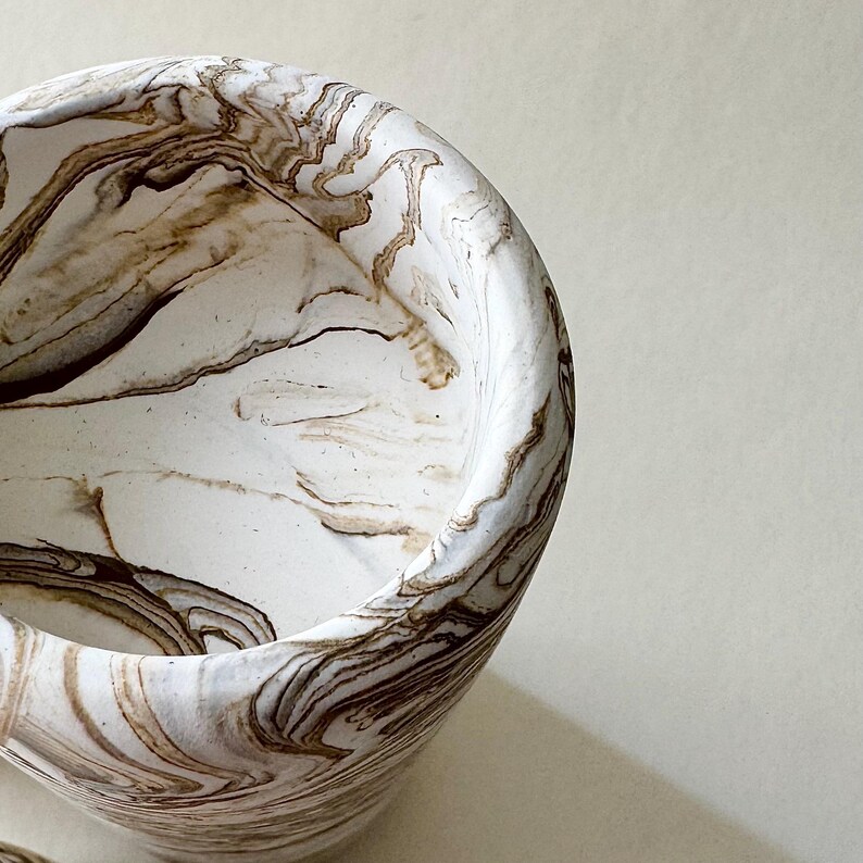 May include: A white bowl with a brown marbled design. The bowl has a rounded shape and a smooth surface. The brown marbling creates a swirling pattern throughout the bowl. This decorative bowl is suitable for home decor.