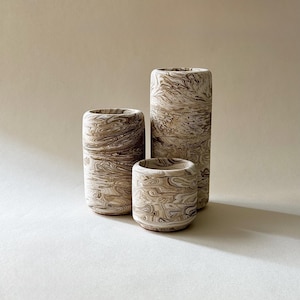 May include: Three cylindrical ceramic vases with a marbled pattern in shades of brown and cream. The vases vary in height, with the tallest being approximately 20 cm tall. The design gives the vases a unique, organic look, suitable for home decor.