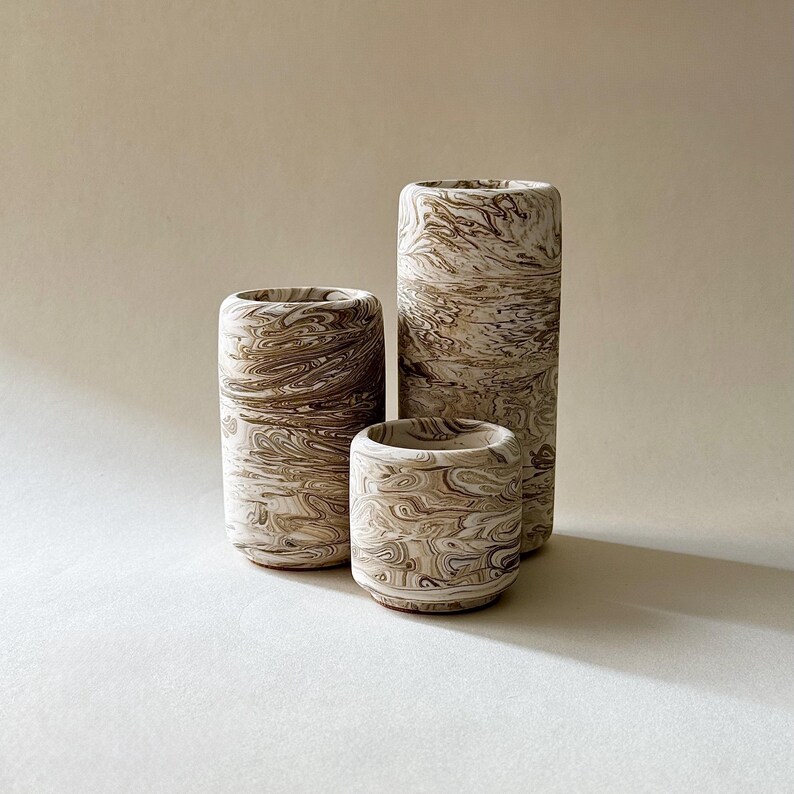 May include: Three cylindrical ceramic vases with a marbled pattern in shades of brown and cream. The vases vary in height, with the tallest being approximately 20 cm tall. The design gives the vases a unique, organic look, suitable for home decor.