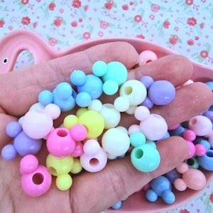 May include: A collection of pastel-coloured plastic beads shaped like Mickey Mouse heads. The beads have a hole in the centre for stringing.