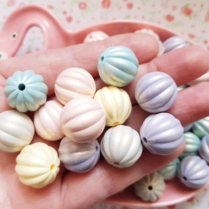 Puede incluir: Una colección de cuentas redondas de plástico de color pastel con una superficie texturizada y nervada. Las cuentas son en tonos de azul, rosa, amarillo y morado.