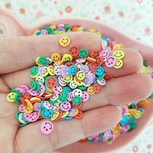 May include: A large assortment of colorful smiley face shaped resin embellishments. The embellishments are in various colors including yellow, green, blue, pink, orange, and red.