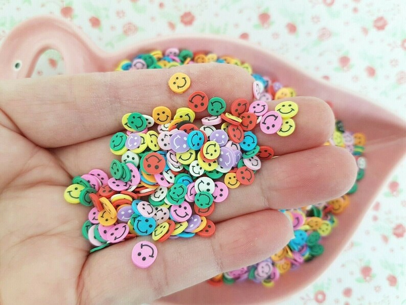 May include: A large assortment of colorful smiley face shaped resin embellishments. The embellishments are in various colors including yellow, green, blue, pink, orange, and red.
