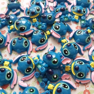 May include: A collection of blue, pink, and yellow Stitch character charms. The charms are made of plastic and have a glossy finish.