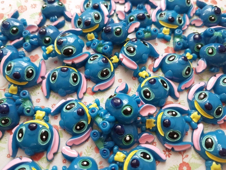 May include: A collection of blue, pink, and yellow Stitch character charms. The charms are made of plastic and have a glossy finish.