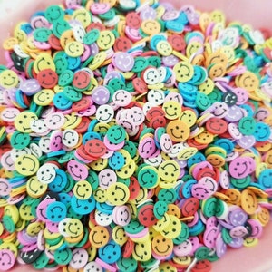 May include: A large pile of colorful smiley face sprinkles. The sprinkles are made of plastic and are in a variety of colors, including yellow, red, blue, green, and pink.