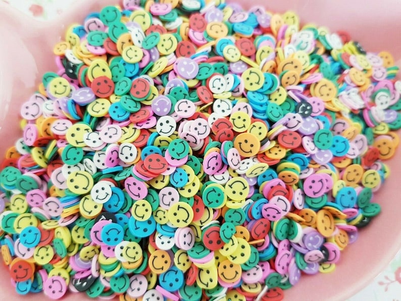 May include: A large pile of colorful smiley face sprinkles. The sprinkles are made of plastic and are in a variety of colors, including yellow, red, blue, green, and pink.