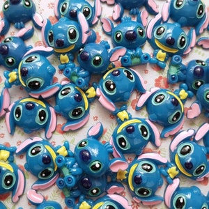 May include: A collection of blue, pink, and yellow Stitch character charms. The charms are made of plastic and have a glossy finish.