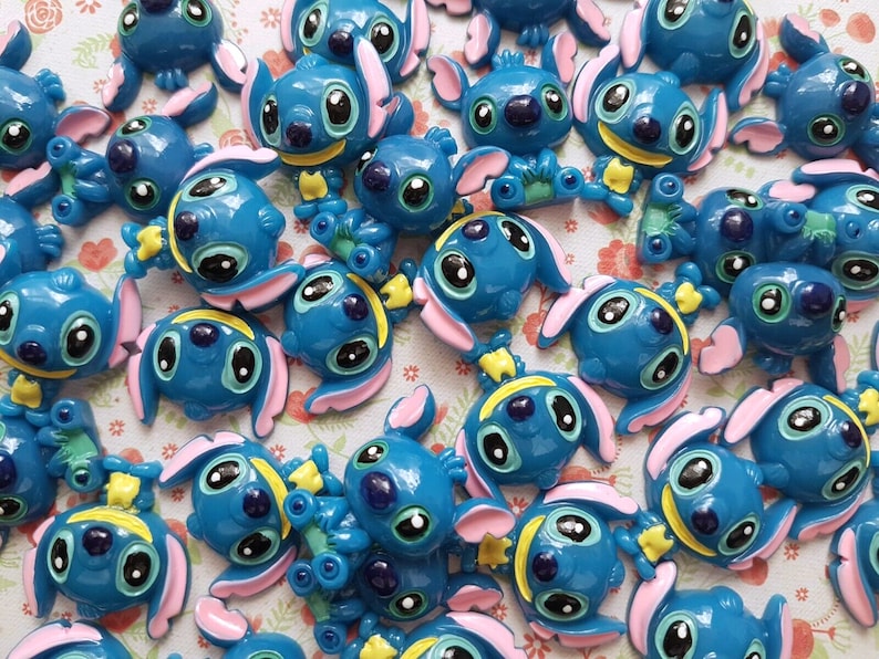 May include: A collection of blue, pink, and yellow Stitch character charms. The charms are made of plastic and have a glossy finish.