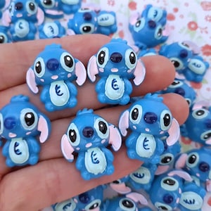 Op de afbeelding: Een verzameling blauwe Stitch-figuurtjes met roze oren en witte ogen. De figuurtjes zijn gemaakt van hars en hebben een glanzende afwerking.