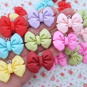 May include: Assortment of colourful bow charms with silver jump rings. The bows are made of polymer clay and come in a variety of colours, including red, pink, blue, yellow, green, and purple.